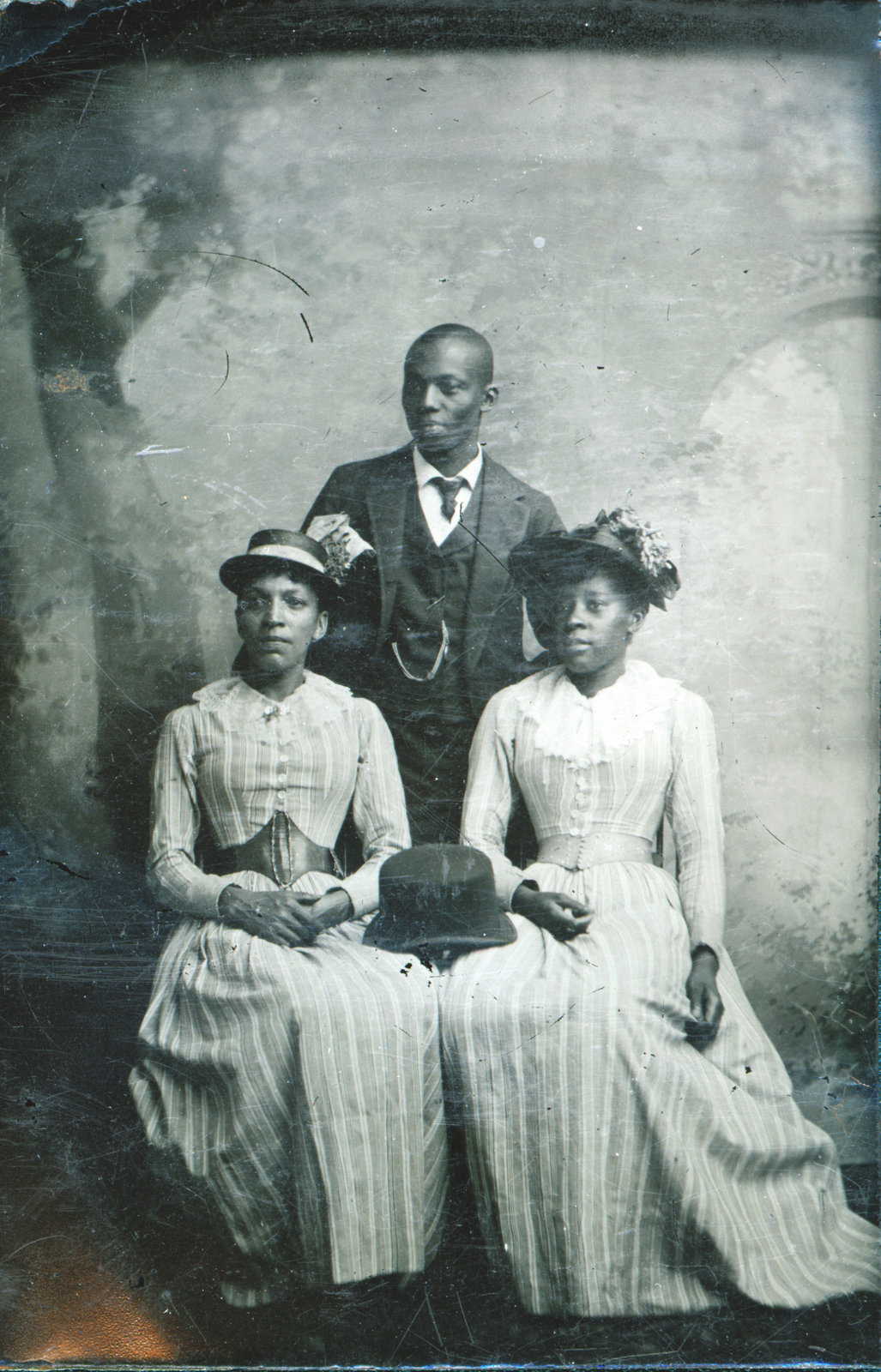 A small tintype of three unidentified individuals, two women, seated, and a young Black gentleman, standing. The date, location and name of the photographer are unknown. Courtesy the Brock University James A. Gibson Special Collections & Archives.