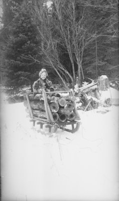 Middle Island: Esther Hartlep sitting on small sleigh of logs.