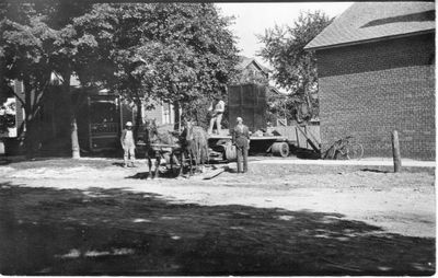 019 Three men working in a residential area with a horse team and open wagon with what looks to be a large safe. Wagon has oversized, heavy-duty wheels.