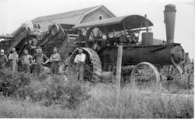 020 Six men standing in front of tractor with farm? equipment attached. Barn in background