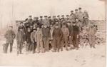 064 Crew of 40 men standing outside lumber camp building in winter