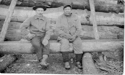 236 Native American John Wastinabee on right, Frenchman on left sitting on log in front of log building.