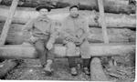 236 Native American John Wastinabee on right, Frenchman on left sitting on log in front of log building.