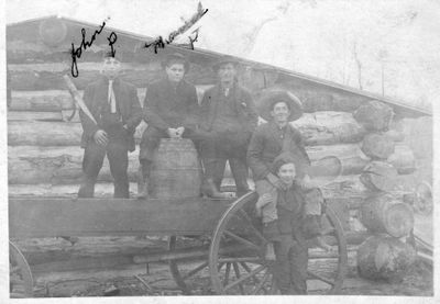 450 Five men posing on wagon outside a lumber camp building