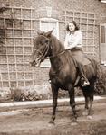 Ruth Morgan on horseback at the side of a red brick house.