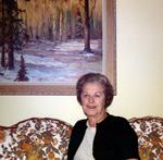 “Ruby Herrington” sitting on the couch. Landscape painting hanging on the wall behind.