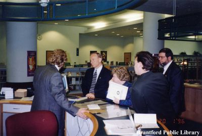 Hon. Marilyn Mushinski, Hon. John Snobelen, and Ron Johnson MPP stand at the Information Desk at the Brantford Public Library