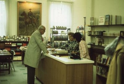 Interior of Carnegie library, checkout desk, reference and film department, 1975