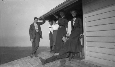 Four women and two men resting on a second floor porch