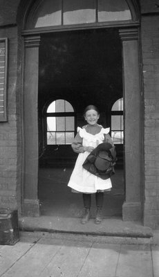 A young girl holding her hat in the doorway of the Grand Truck Railroad Station