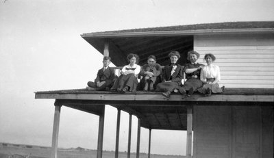 A group of young women and men sitting on a porch roof