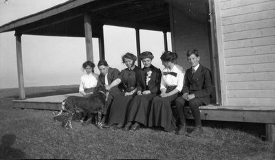 A group of young women and men sitting on a porch with a dog