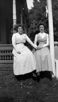 Two young women sitting on a fence in front of house