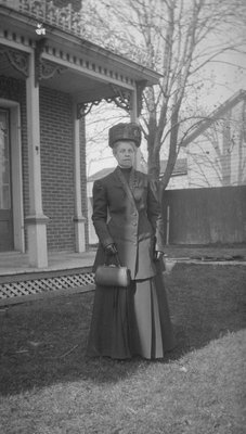 A woman in formal dress standing in front of a house