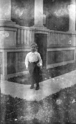 A young Griffis? boy standing outside in front of a house