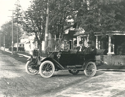 A young boy driving two men,possibly Frank Griffis and Chief Jamieson, in a 1910s car