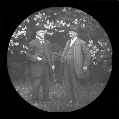 Two men standing in front of blooming lilac bushes