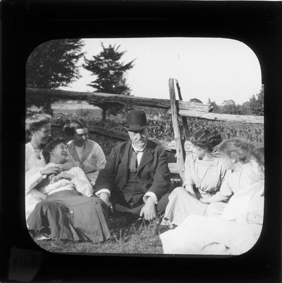 Six young women and a man sitting by a split rail fence