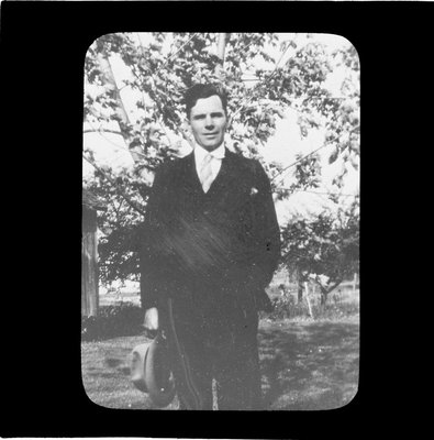 A man standing in yard holding his hat