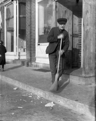 A man sweeping the sidewalk outside the Post Office, Colborne