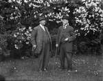 Two men standing in front of blooming lilac bushes