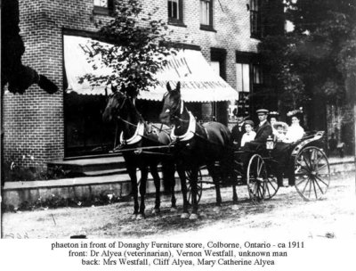 Dr. James Alyea, Mrs. Alfreda Westfall, Cliff Alyea, and Mrs. Mary Catherine Alyea in front of Donaghy’s furniture and picture framing shop, Colborne, Cramahe Township