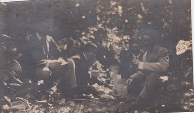 Postcard of a group of men in the woods, inscribed with Gertie Mikle's initials