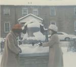 Library bell cairn on Church Street - two nurses from the Philippines play with the snow.