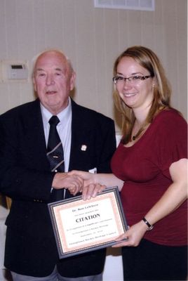 A woman accepting Dr. Ron Lefebvre's citation from Georgetown Hockey Heritage Council