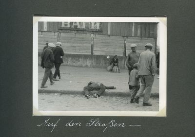 A famine victim lies dead near a market in Kharkiv with some men pausing to look while others pass by