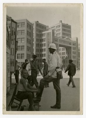 A traffic officer is getting a shoeshine from a young boy with the new Kharkiv government buildings in the background