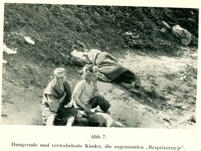 Two destitute children sit near a sleeping woman by a grassy embankment in Kharkiv