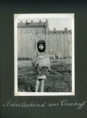 A thin young girl faces the camera as she stands near a factory in Kharkiv