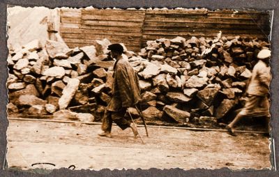 A barefoot young man on crutches walks past a pile of stone rubble on a street in Kharkiv