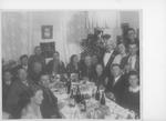 Several men and women pose around a dinner table laden with food and drinks