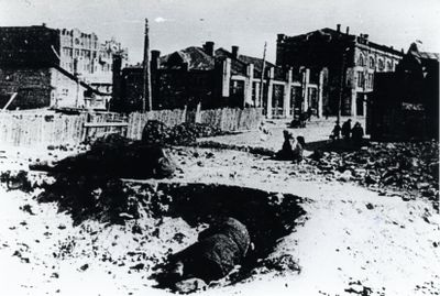 A person lies in a partially excavated area in Kharkiv with old factory buildings in the background