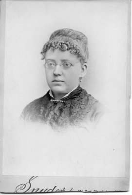 Head and shoulder portrait of an unidentified young woman with tight curled bangs and glasses.