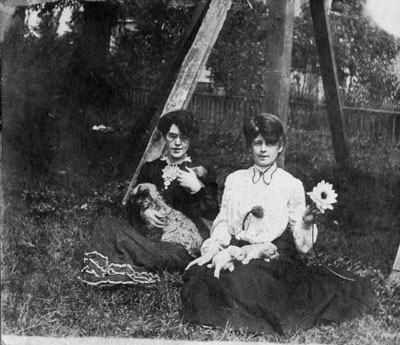 Two ladies sitting by by trees with dog and puppies.