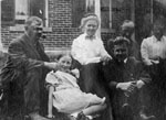 Family group of six seated in front of brick house