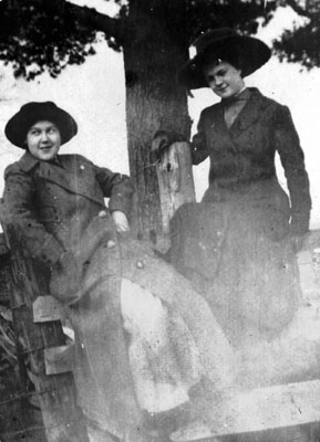 Two young ladies seated by tree