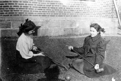 Two young ladies seated on grass holding croquet mallets