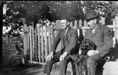 Two men and dog sitting by fence