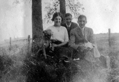 Two men and one young woman posed by tree