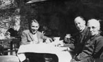 Two men and an elderly lady seated at table outdoors.