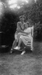 Two young ladies sharing chair in garden.