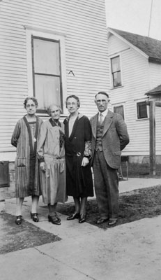 Three women and one man posed in front of house