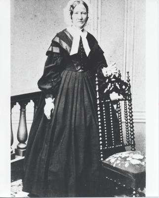 Senior woman standing behind dark wood chair.