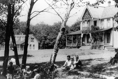 Children and youth on lawn, and Lucy Maud Montgomery on veranda in background