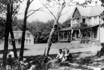 Children and youth on lawn, and Lucy Maud Montgomery on veranda in background