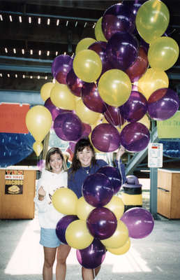 Two women holding purple and yellow balloons